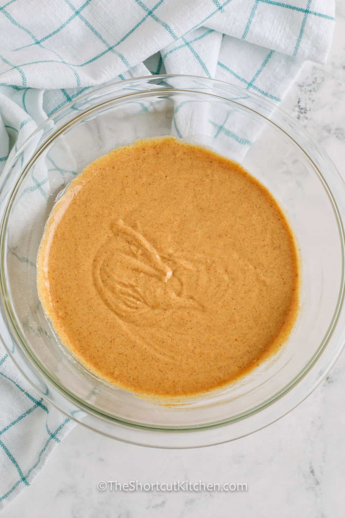 This easy pumpkin roll cake is soft, creamy, and filled with cozy pumpkin spice flavor. Canned pumpkin and yellow cake mix make the cake simple to prepare, while cream cheese and whipped topping create a fluffy filling. Roll the warm cake in a powdered sugar towel, cool, fill, and chill for beautiful slices. Add this cake mix pumpkin roll to your Thanksgiving dessert menu and save the recipe today. #theshortcutkitchen mixed ingredients in bowl to make Pumpkin Roll Cake.