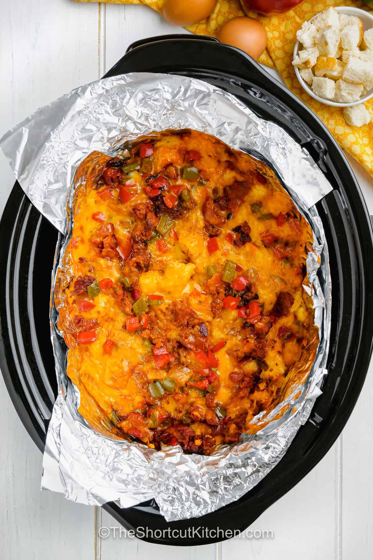 Make Slow Cooker breakfast strata when you need a savory breakfast that can feed a hungry family or brunch crowd. French bread absorbs a rich egg and half-and-half custard while chorizo, peppers, cumin, chili powder, and sharp cheddar add plenty of flavor. This easy slow cooker breakfast casserole also keeps valuable oven space free for other dishes. Pin this cozy breakfast recipe for later. #theshortcutkitchen cooked slow cooker breakfast casserole in a slow cooker with an aluminum foil sling.