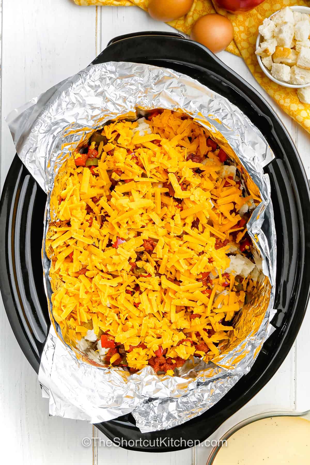 Slow Cooker breakfast strata is an easy, hearty brunch casserole layered with French bread, smoky chorizo, red and green bell peppers, sharp cheddar, and creamy eggs. Drying the bread first gives this crockpot breakfast casserole a tender texture without getting soggy. Let the slow cooker do the work, then add avocado, tomato, sour cream, and cilantro before serving. Save this recipe for your next weekend brunch. #theshortcutkitchen More layers of unmelted cheese over the slow cooker breakfast strata casserole.