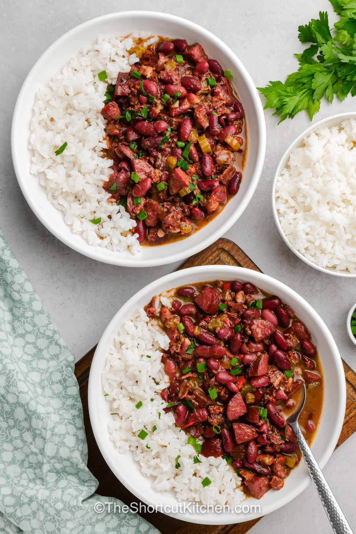 Make easy red beans and rice when a hearty, smoky comfort food dinner is calling. Dried kidney beans slowly simmer with andouille sausage, bacon, peppers, celery, thyme, cayenne, and chicken broth until tender and full of flavor. Serve this red beans and rice with sausage over hot white rice and finish it with fresh green onions. Pin this recipe for your next cozy dinner. #theshortcutkitchen bowls of Easy Red Beans and Rice.