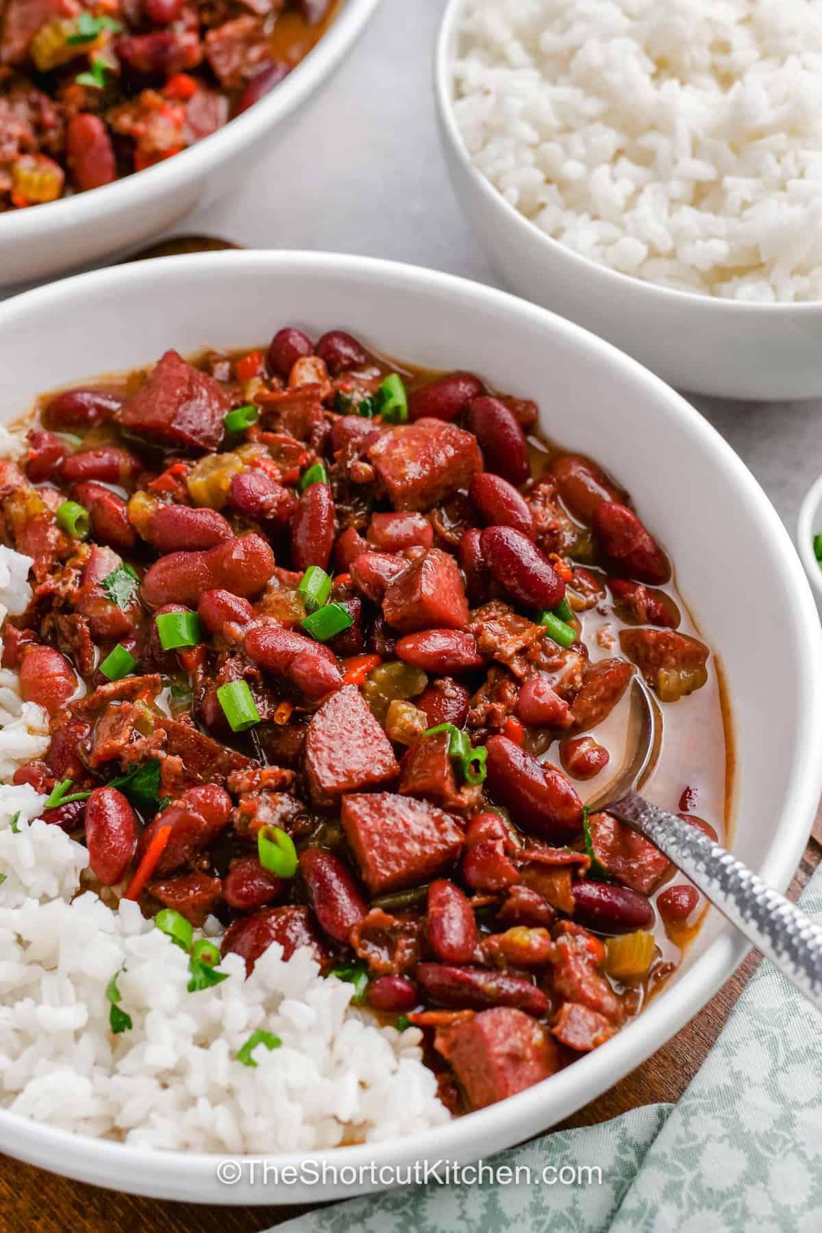 Easy red beans and rice is a hearty stovetop dinner made with dried kidney beans, smoky andouille sausage, bacon, onion, celery, peppers, and savory seasonings. Everything simmers gently in chicken broth until the beans are tender and creamy, then gets spooned over fluffy white rice. Save this comforting red beans and rice recipe for a cozy family dinner and make it this week. #theshortcutkitchen close up of Easy Red Beans and Rice in a bowl.