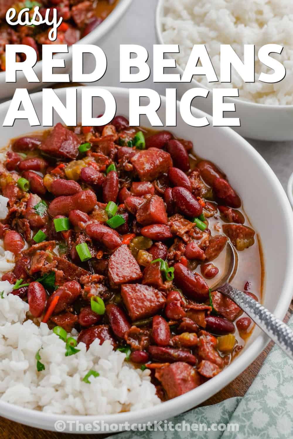 For a hearty family dinner, make this easy red beans and rice recipe with dried kidney beans and smoky andouille sausage. Bacon, peppers, celery, herbs, and chicken broth add layers of flavor while a slow stovetop simmer gives the beans their tender texture. Serve the finished red beans and rice with green onions and extra hot sauce. Save this easy comfort food recipe for your next meal plan. #theshortcutkitchen Easy Red Beans and Rice in a bowl with writing.