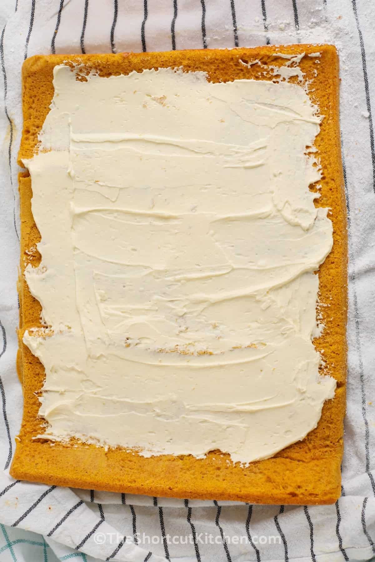 Make a beautiful pumpkin roll cake without baking a cake completely from scratch. Yellow cake mix keeps the ingredient list short while canned pumpkin and pumpkin pie spice add cozy fall flavor. A light cream cheese and whipped topping filling makes every chilled spiral slice creamy and delicious. This easy pumpkin roll is perfect for Thanksgiving or autumn entertaining. Save the recipe for your next fall gathering. #theshortcutkitchen Pumpkin roll cake topped with cream cheese filling